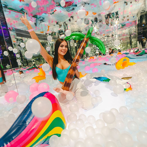 a girl in a giant ball pit sitting on an inflatable palm tree