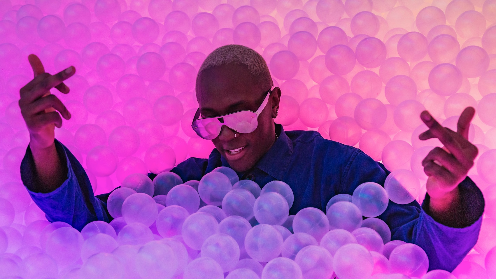 a man sitting in a multicoloured ball pit with his middle fingers up