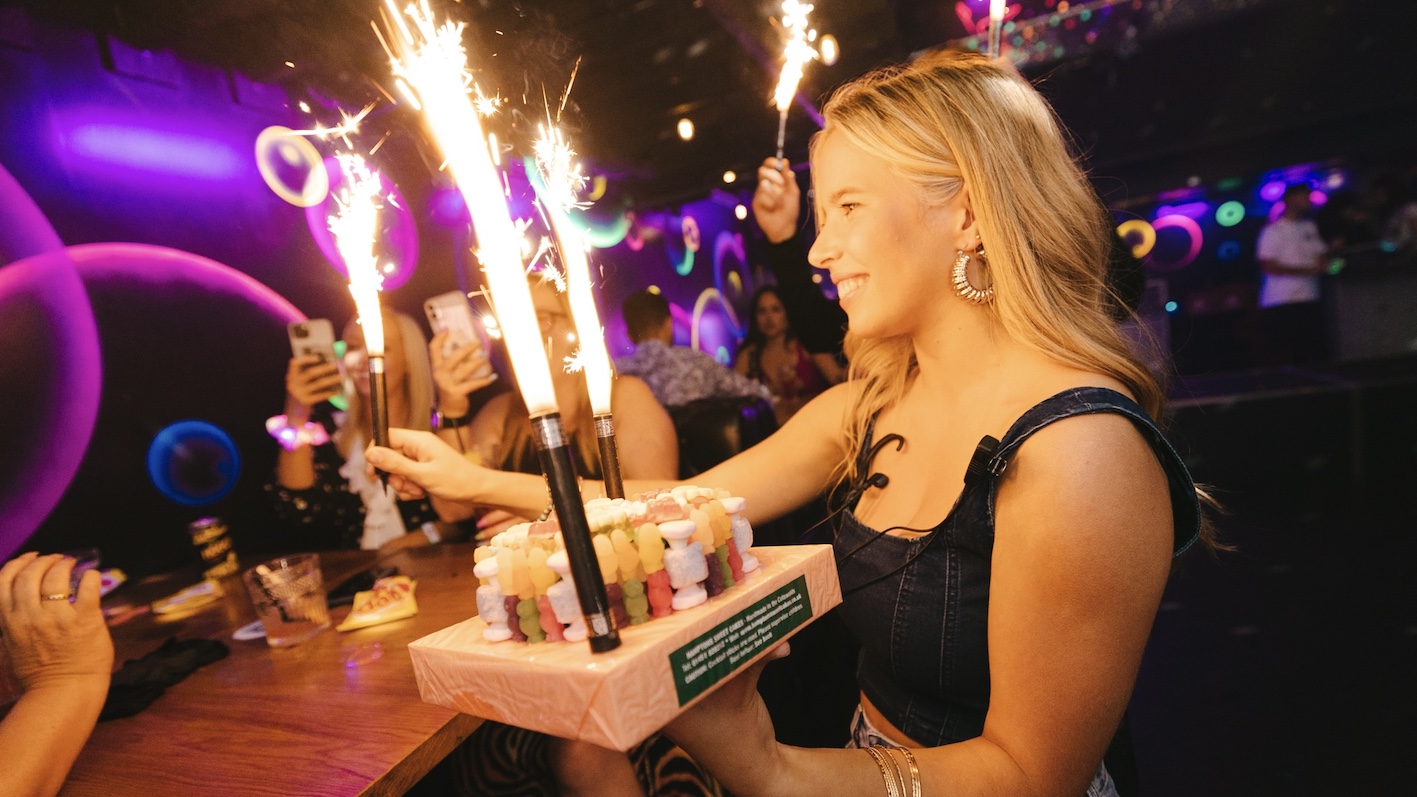 a girl carrying a VIP sweet cake to a table celebrating their birthday
