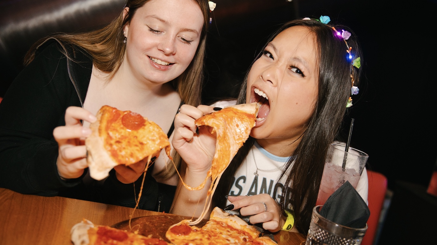 two girls eating pizza and singing