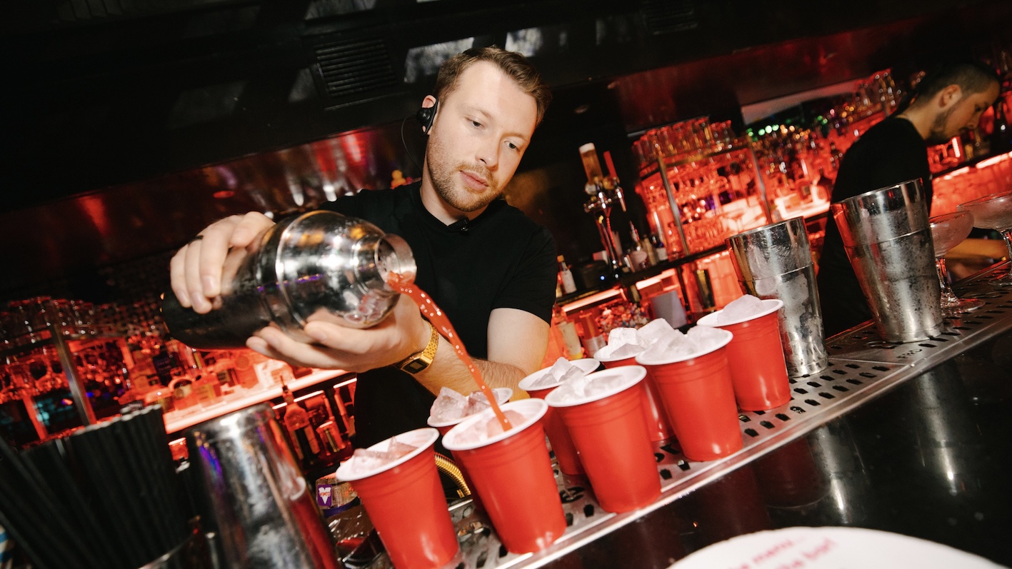 a bartender pouring alcohol into lots of red cups