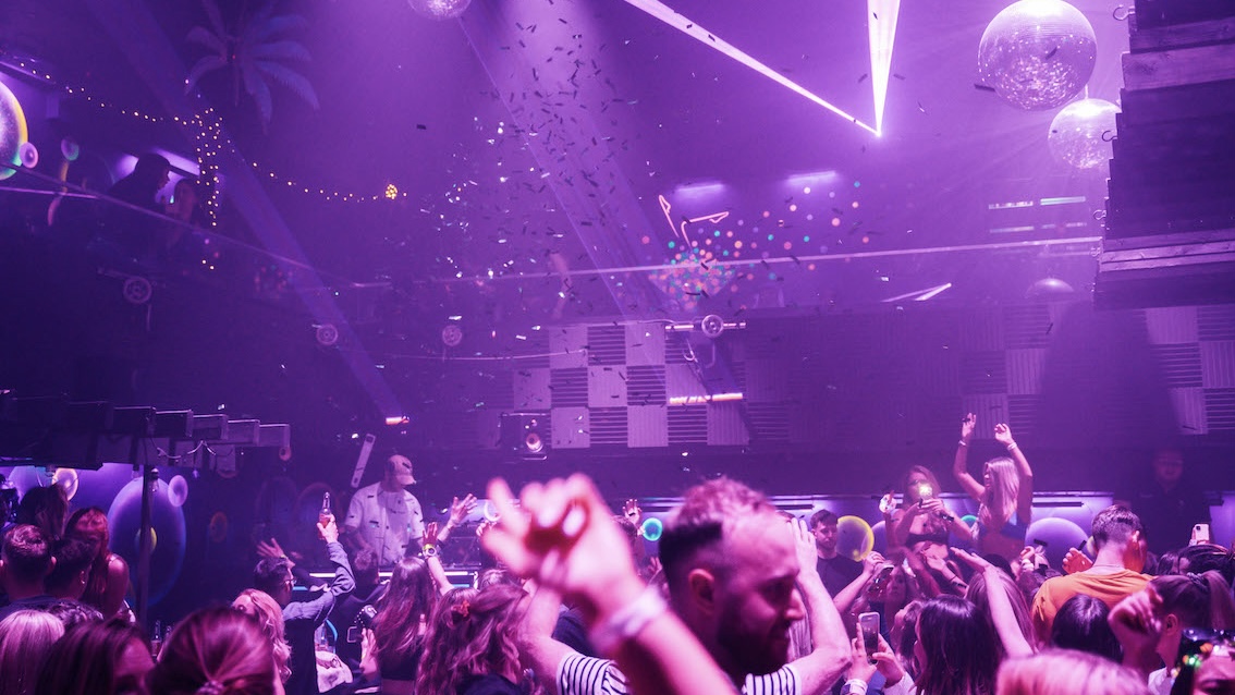 a full dance floor with people partying, listening to the DJ and confetti falling from the ceiling