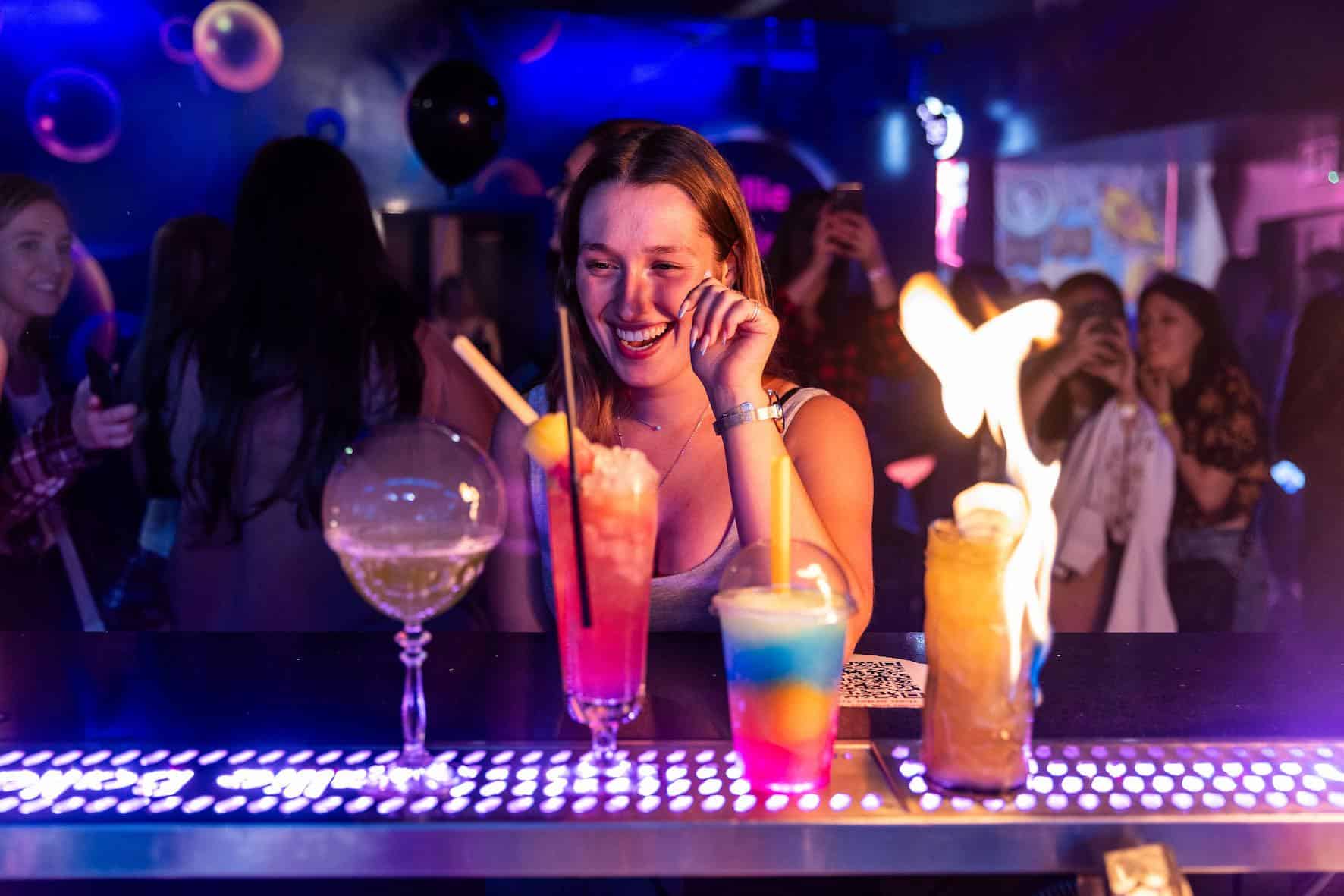 a girl looking at 4 cocktails on the bar in front of her