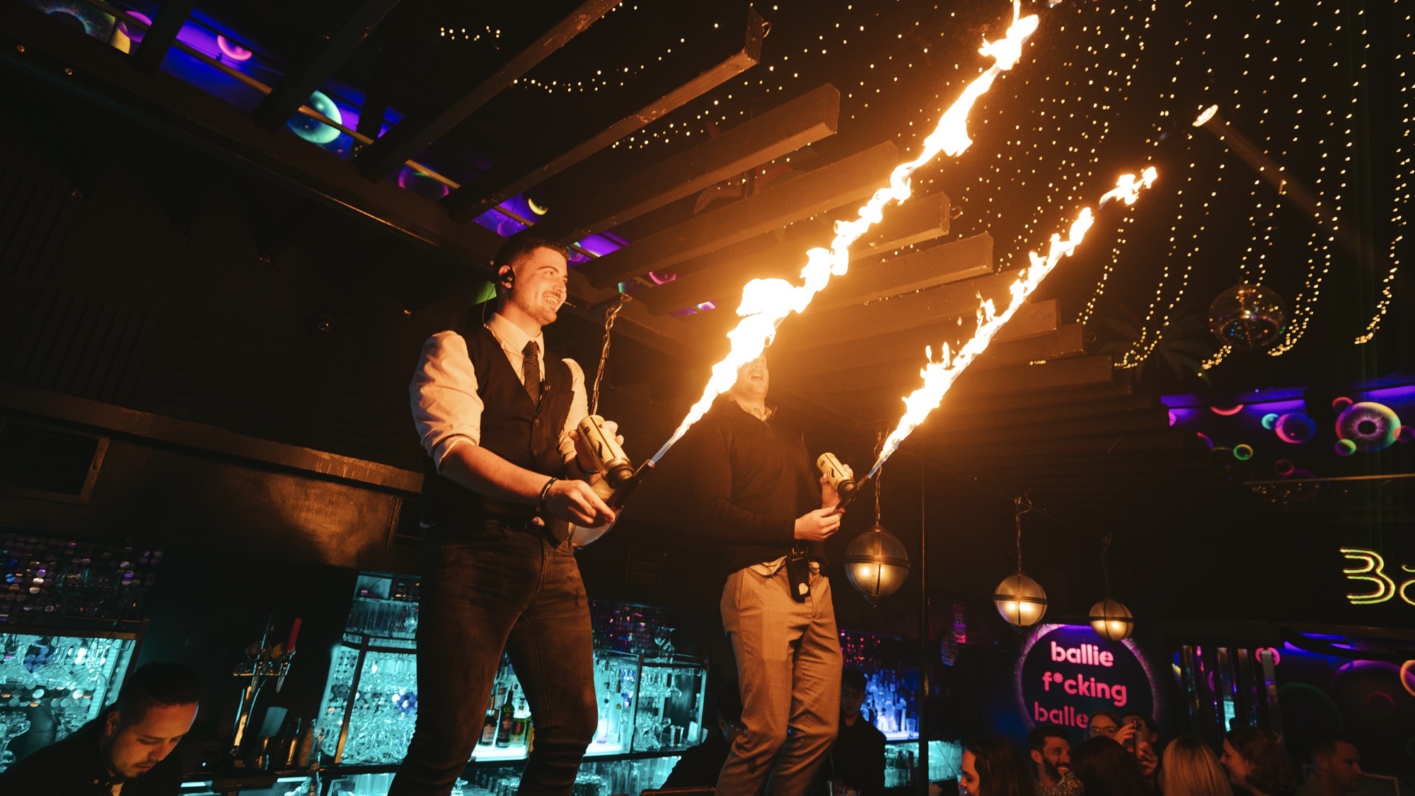 two bartenders stood on the bar with giant sparkler flames