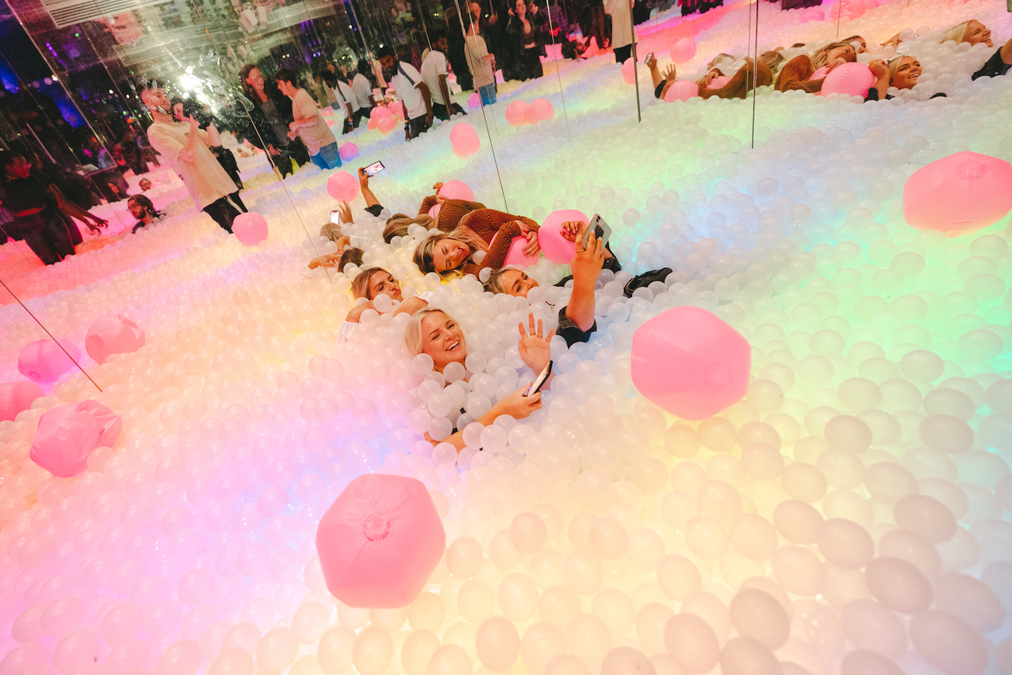 a group of women playing in a ball pit with giant pink inflatables around them