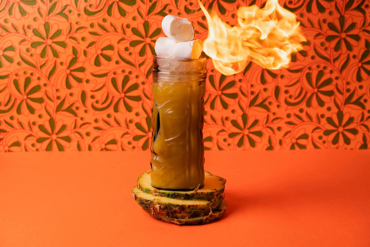 a cocktail with marshmallows on top being roasted by a giant flame