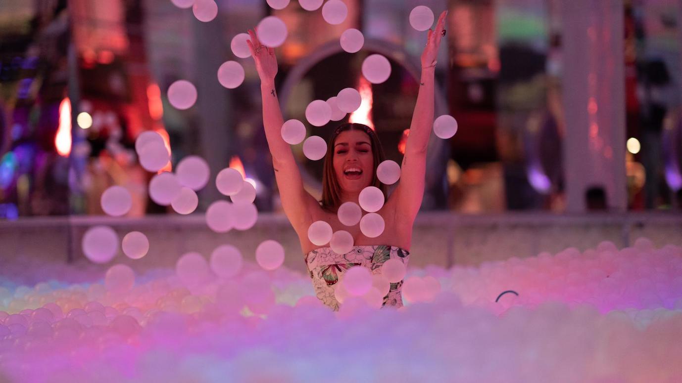 woman smiling in glowing ball pit and throwing plastic balls into the air
