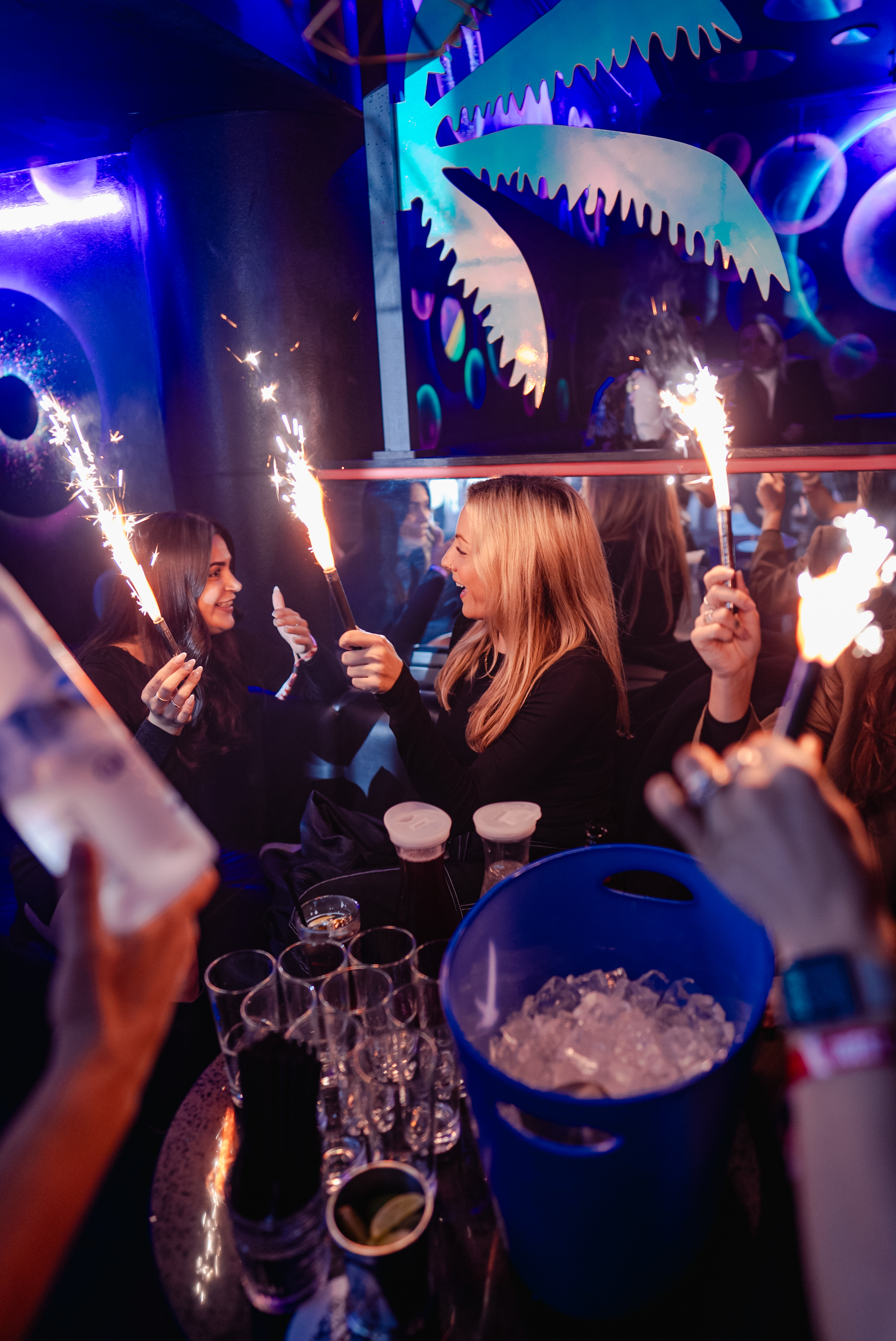 a group of men dancing in a VIP booth, having a bottle of champagne sprayed over them