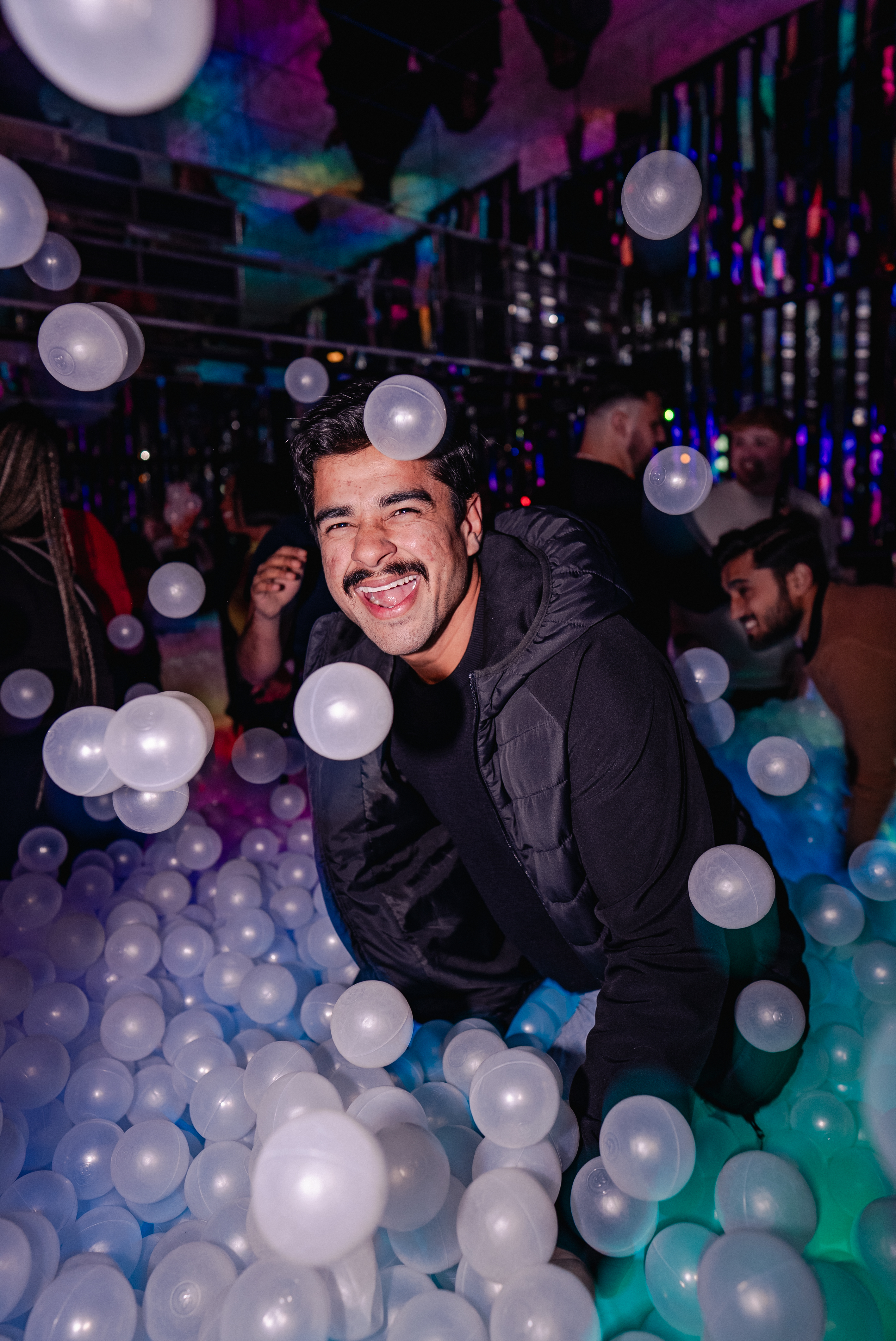 Man in blue shirt in rainbow ball pit throwing balls up