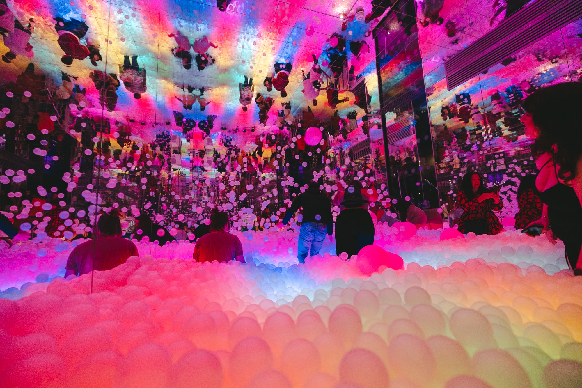 woman smiling in glowing ball pit and throwing plastic balls into the air