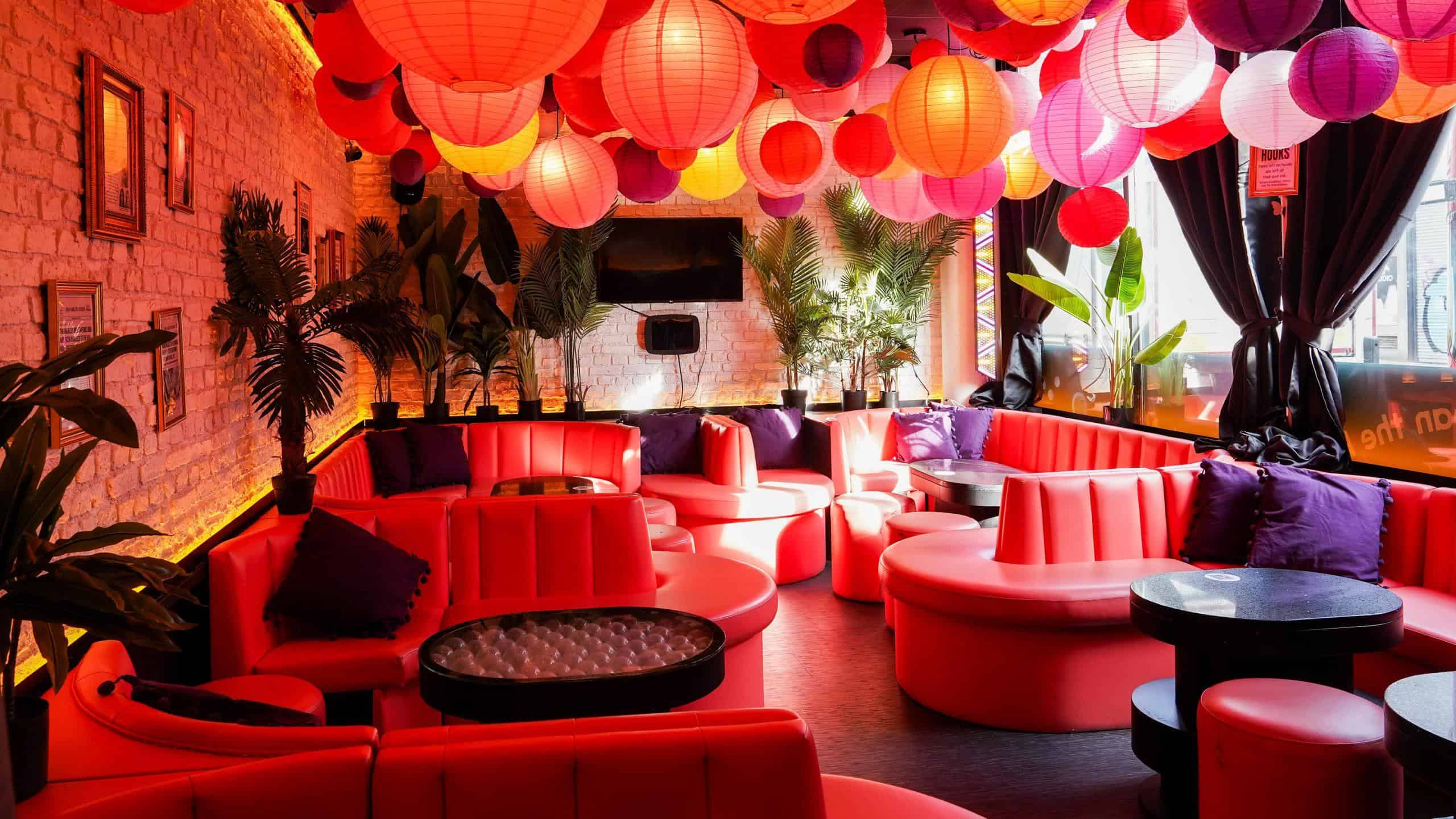 Vibrant indoor bar with red seating, colourful paper lanterns, and lush green plants at Ballie Ballerson London.