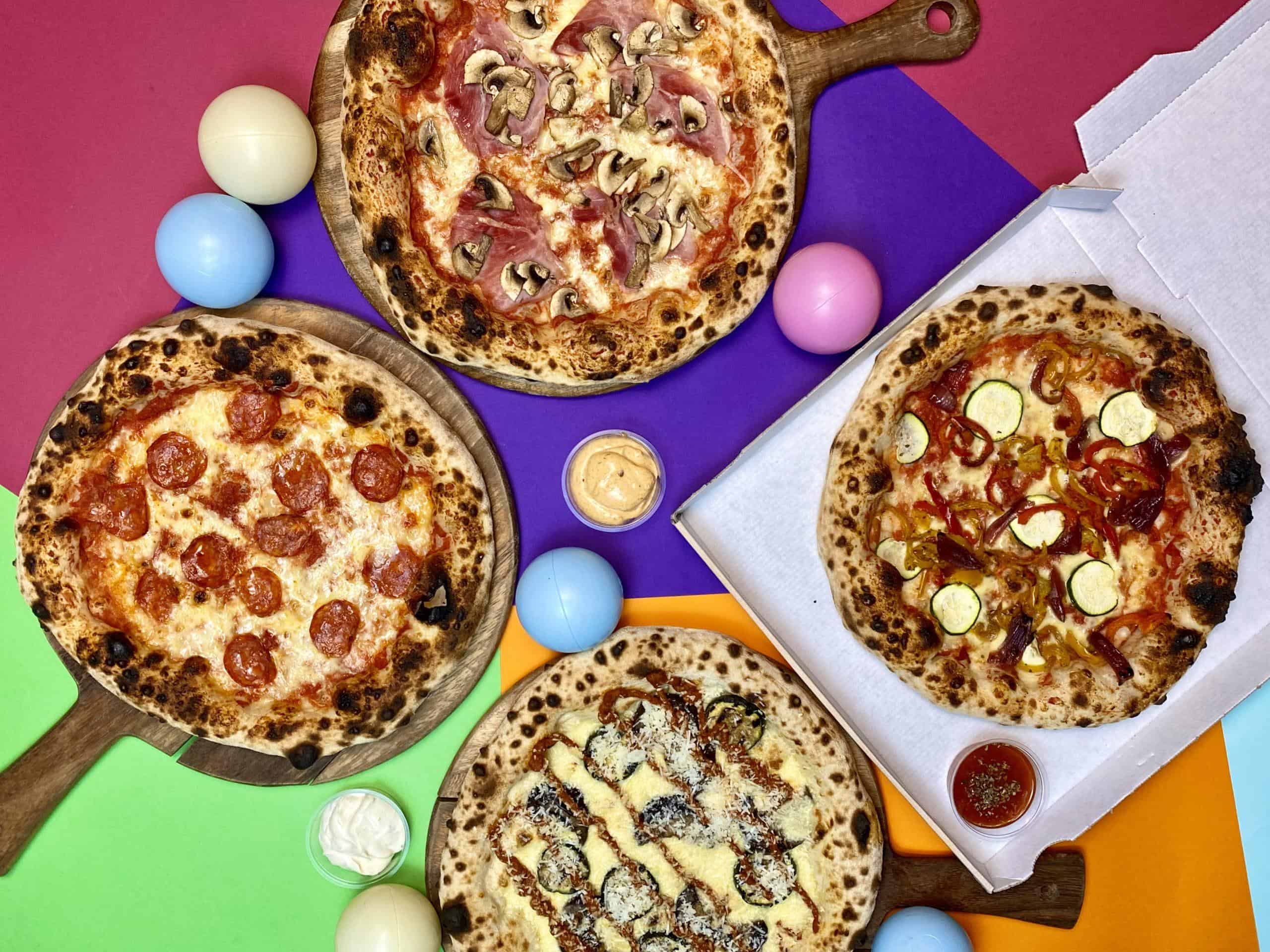 Delicious assorted pizzas on wooden boards with colourful Easter eggs and dipping sauces, perfect for a vibrant pizza party.