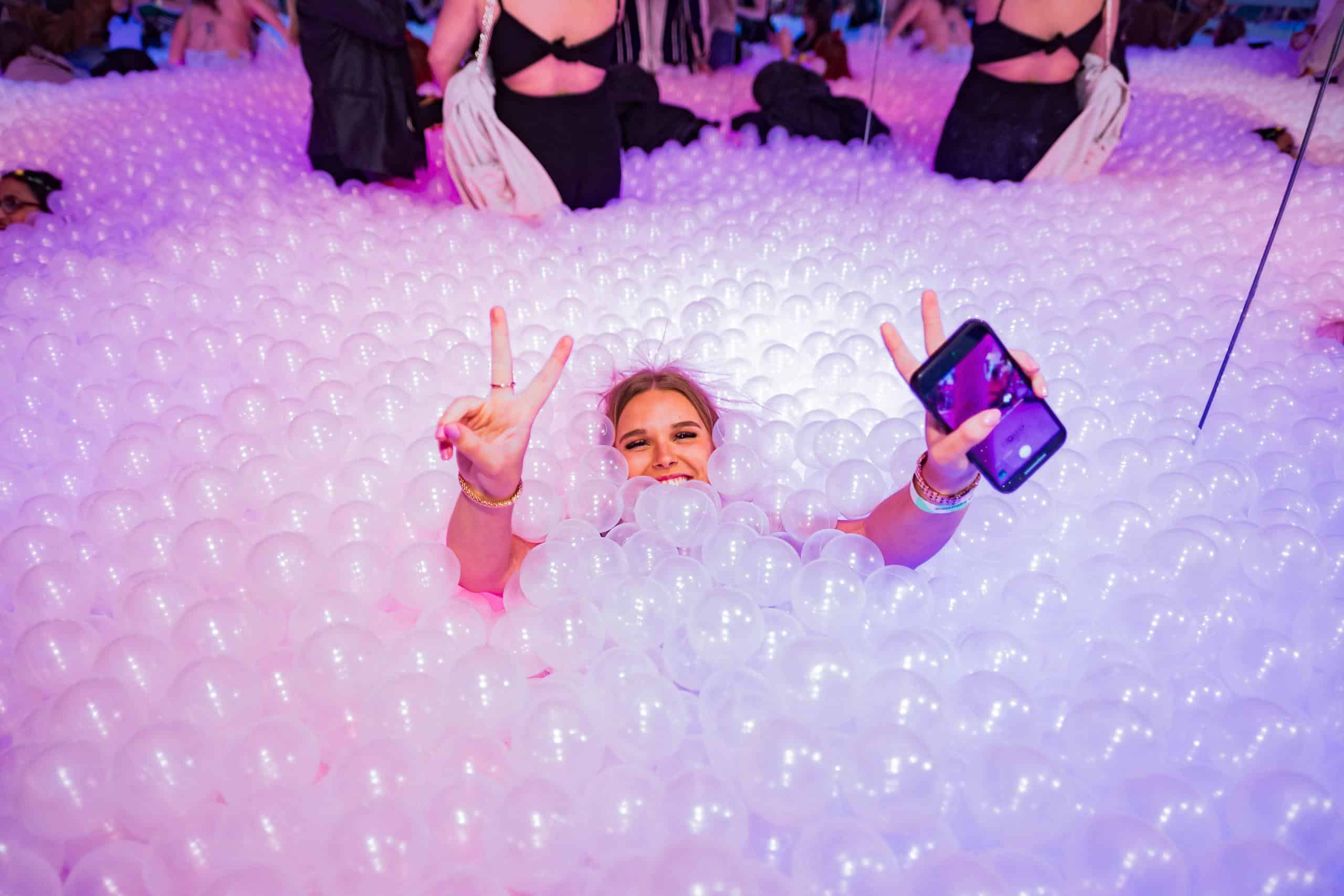 Vibrant ball pit with party guests, colourful lighting, fun atmosphere at Ballie Ballerson.