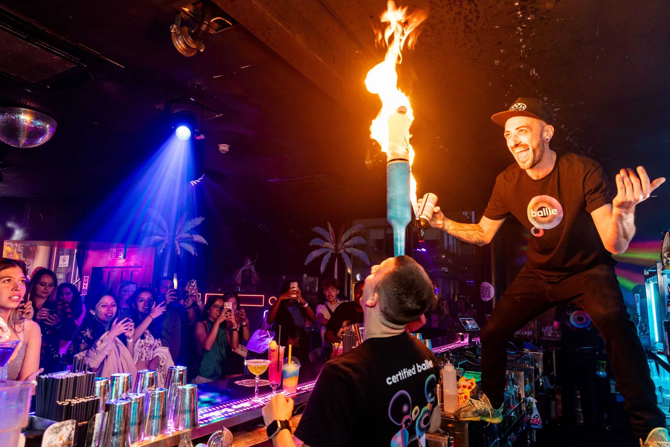 Vibrant nightclub scene at Ballie Ballerson with fire performer entertaining guests in colourful lighting.