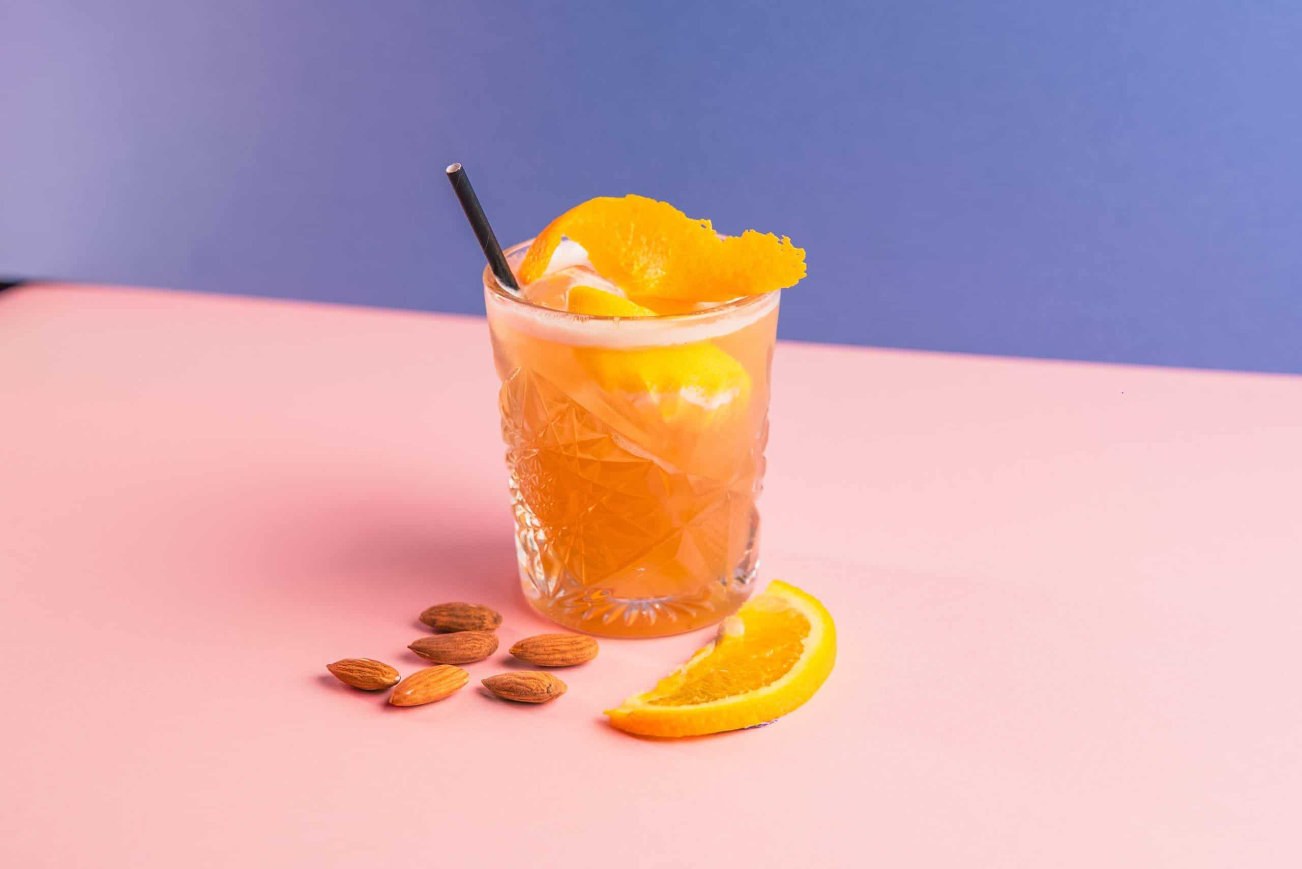 Refreshing orange cocktail with citrus slices and almonds on a colourful table at Ballie Ballerson.